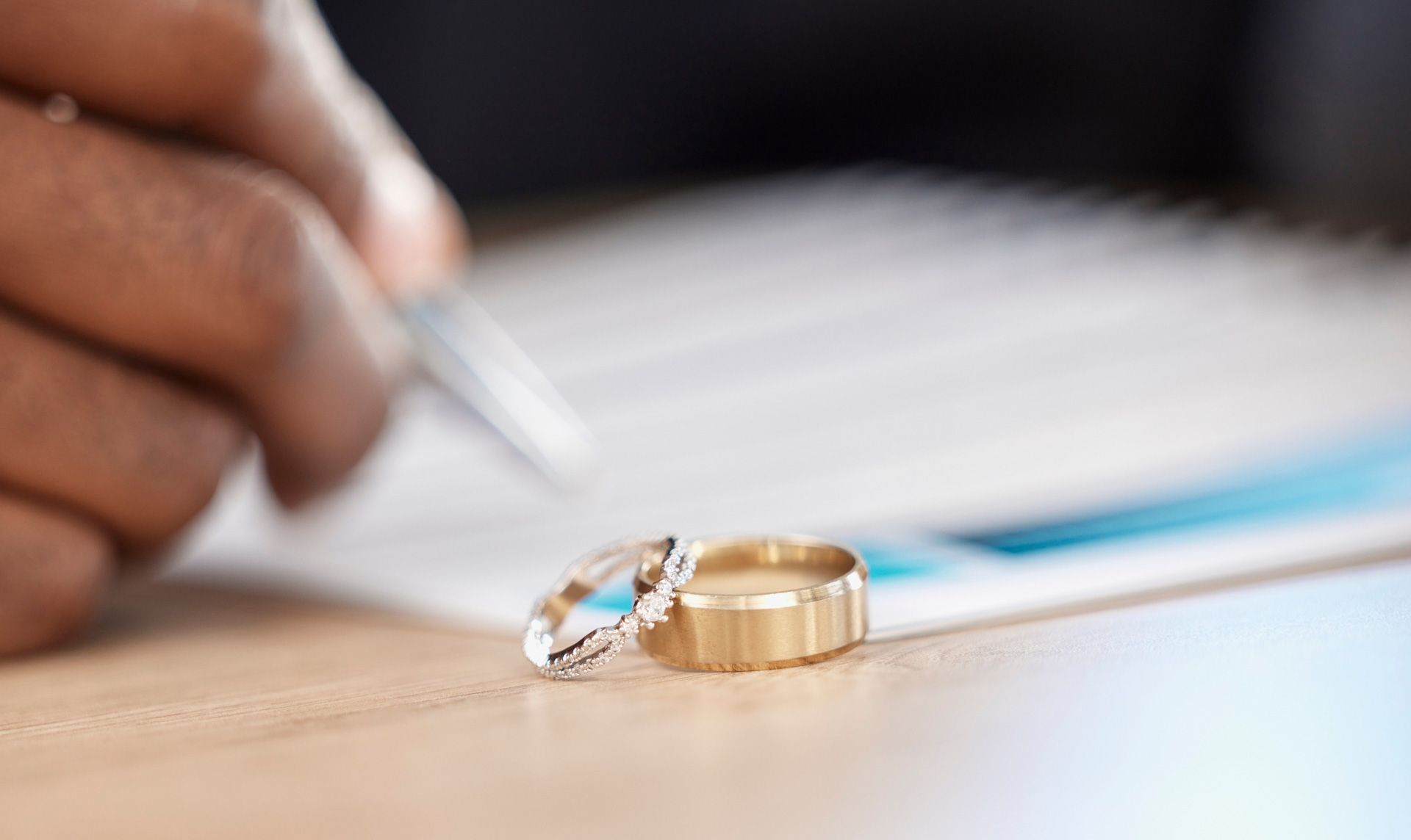 A couple of wedding rings are sitting on a table next to a person signing a document.