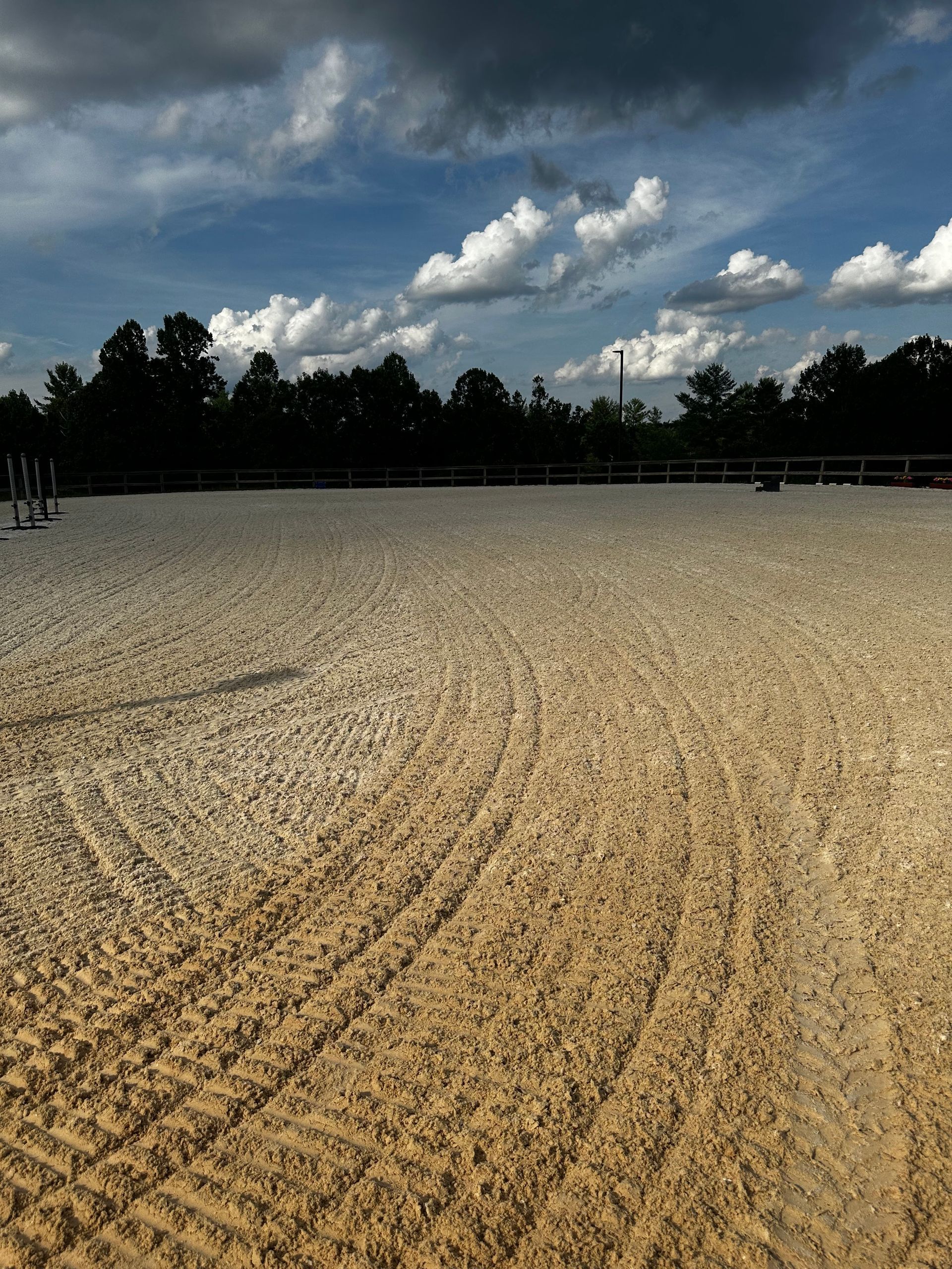 A large sandy field with trees in the background and a cloudy sky.