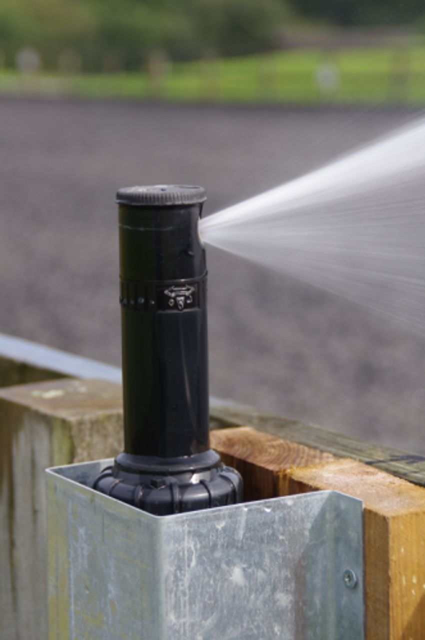 A sprinkler is spraying water on a wooden post.