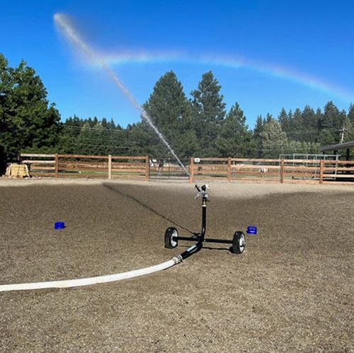 A sprinkler is spraying water on a dirt field with a rainbow in the background.
