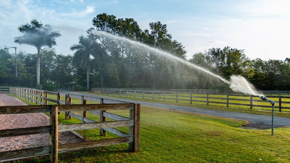 A sprinkler is spraying water on a grassy field next to a wooden fence.