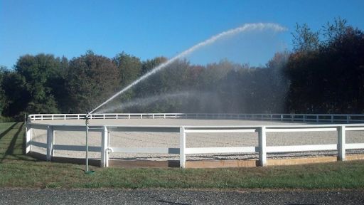 A fenced in area with a sprinkler spraying water on it.