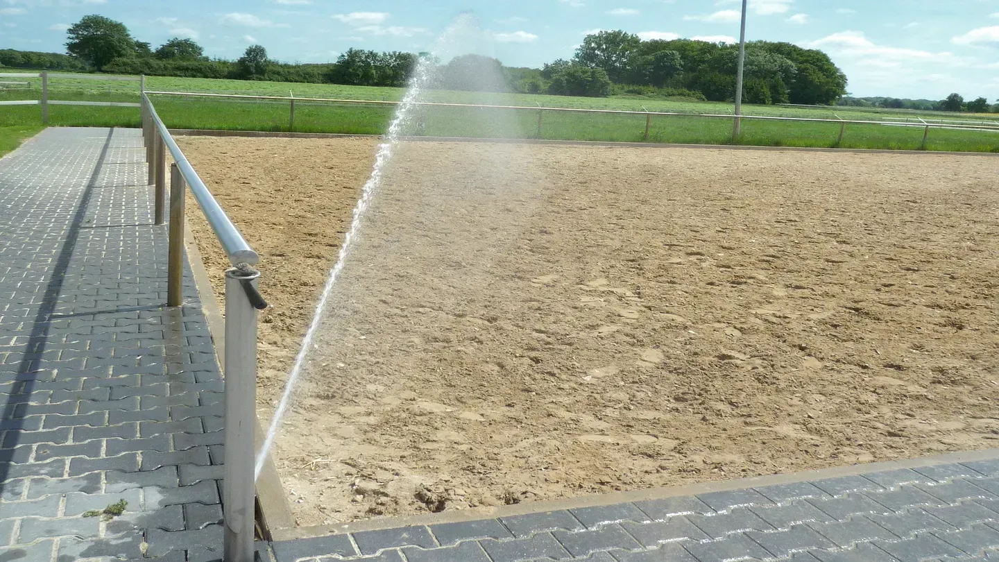 A sprinkler is spraying water on a dirt field.