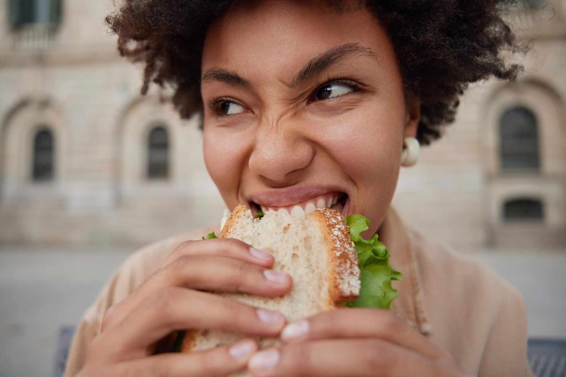 Person biting a sandwich outdoors in front of a historic building