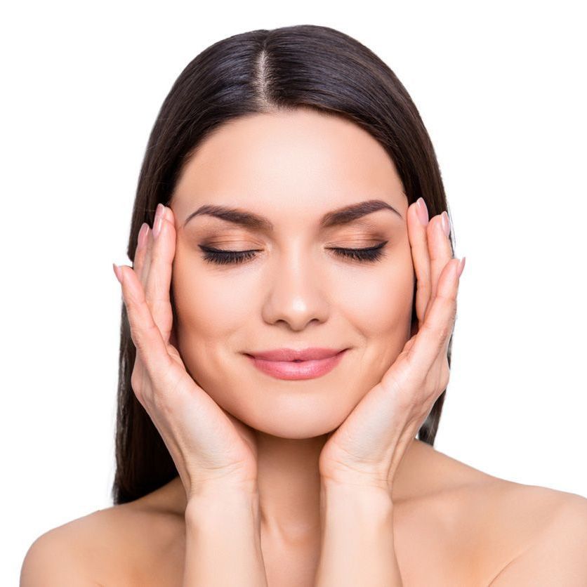 Woman with closed eyes gently touching her face, smiling against a white background