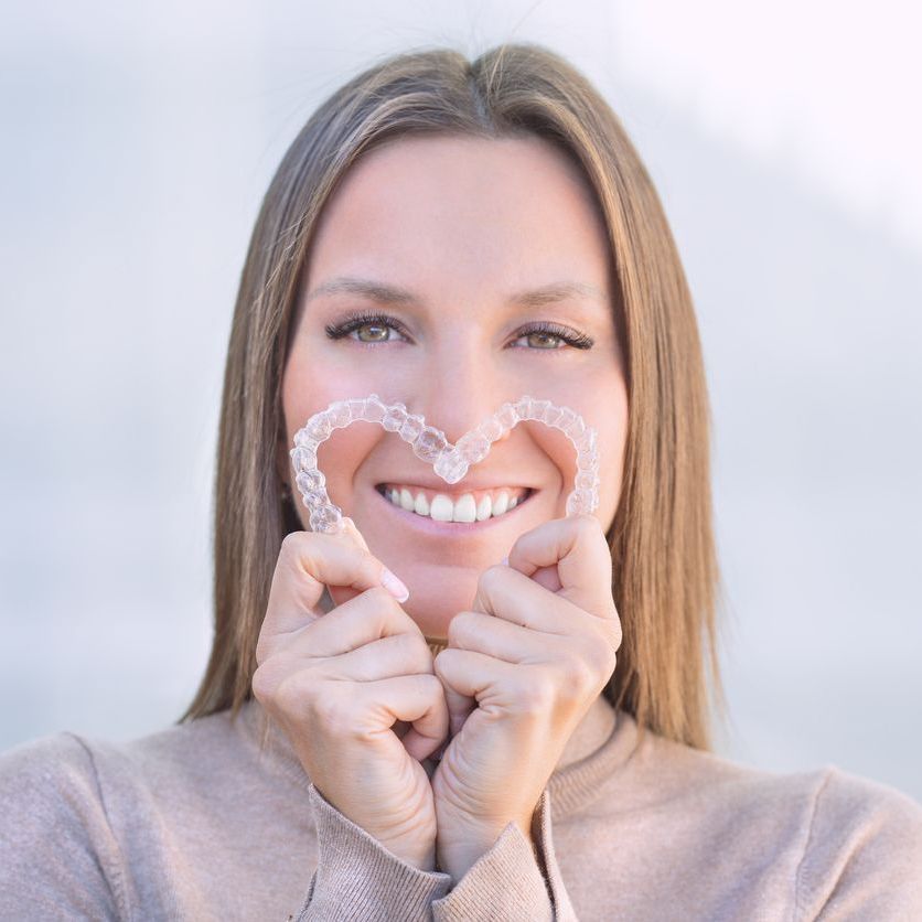 Woman smiling while holding a heart-shaped dental aligner to her face