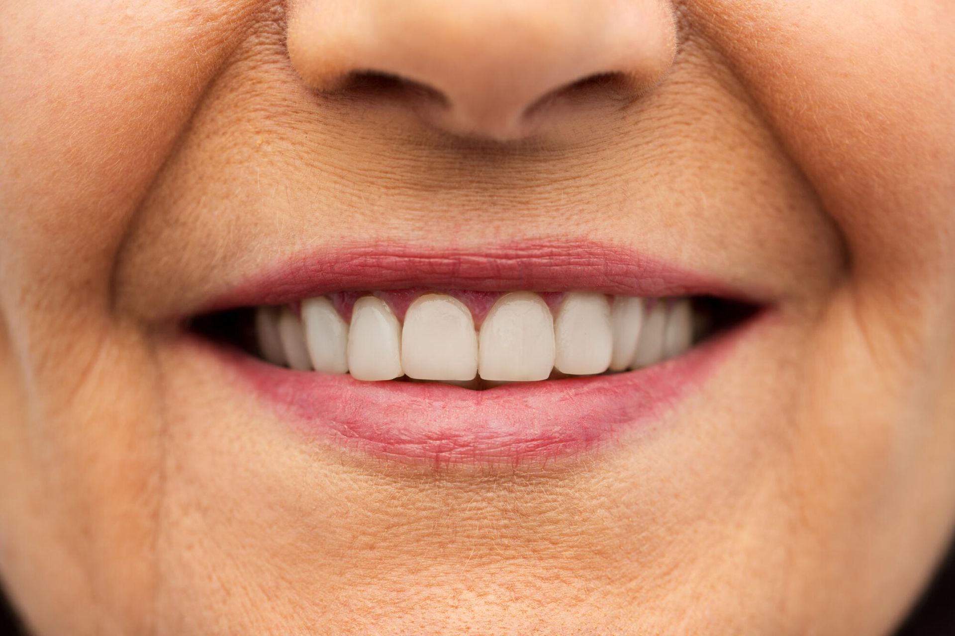 Close-up of a smiling mouth with teeth visible and pink lipstick