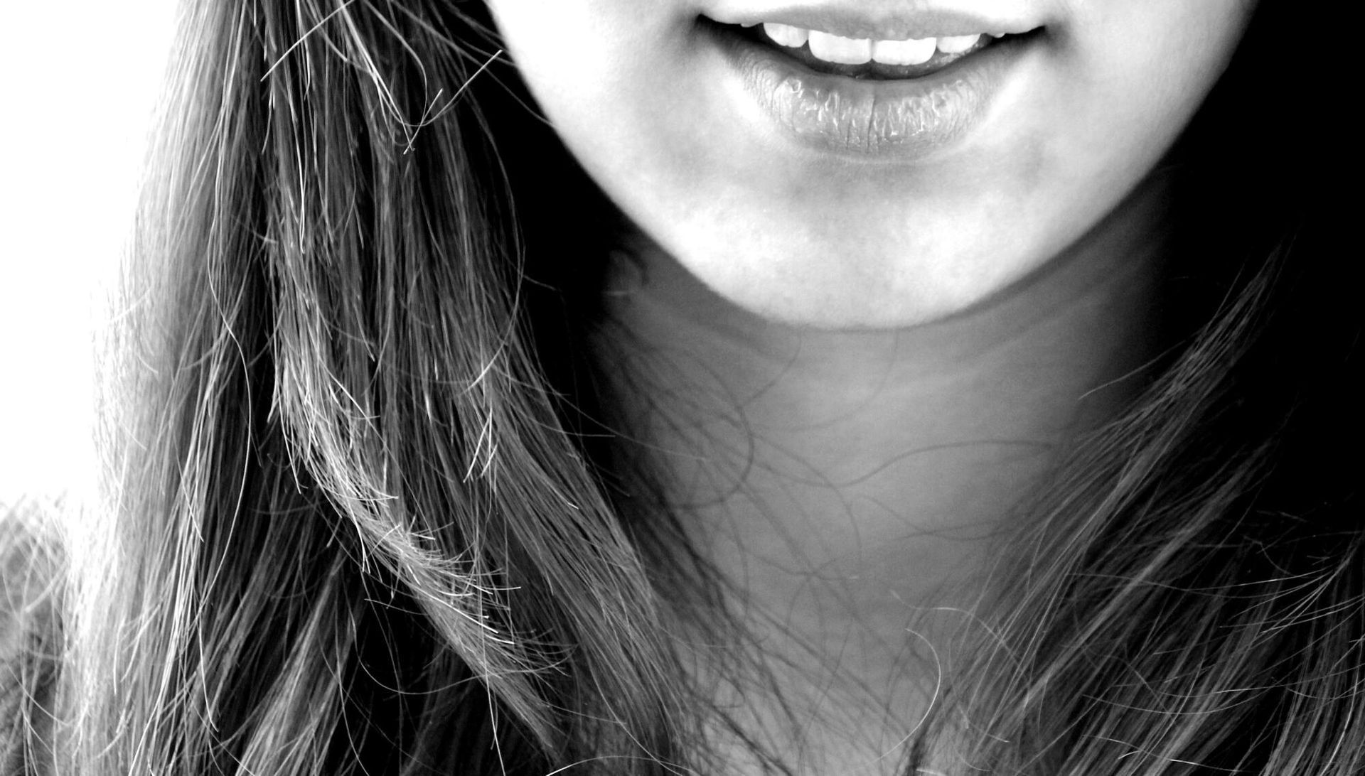 Smiling mouth and chin of a person, long hair framing the face. Black and white photo.