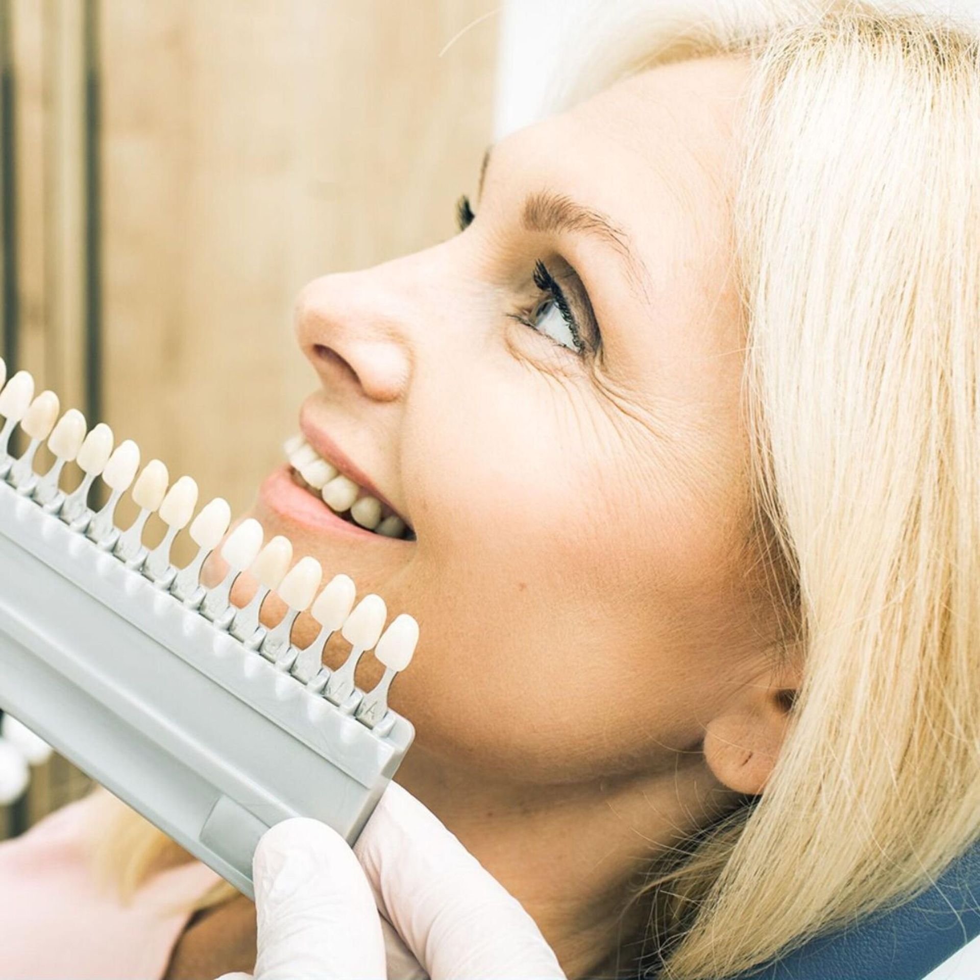 Blonde woman smiling while holding a dental shade guide near her face