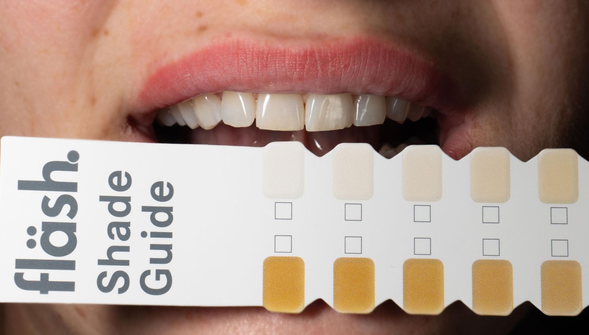 Close-up of a mouth holding a Fläsch shade guide for teeth whitening comparison