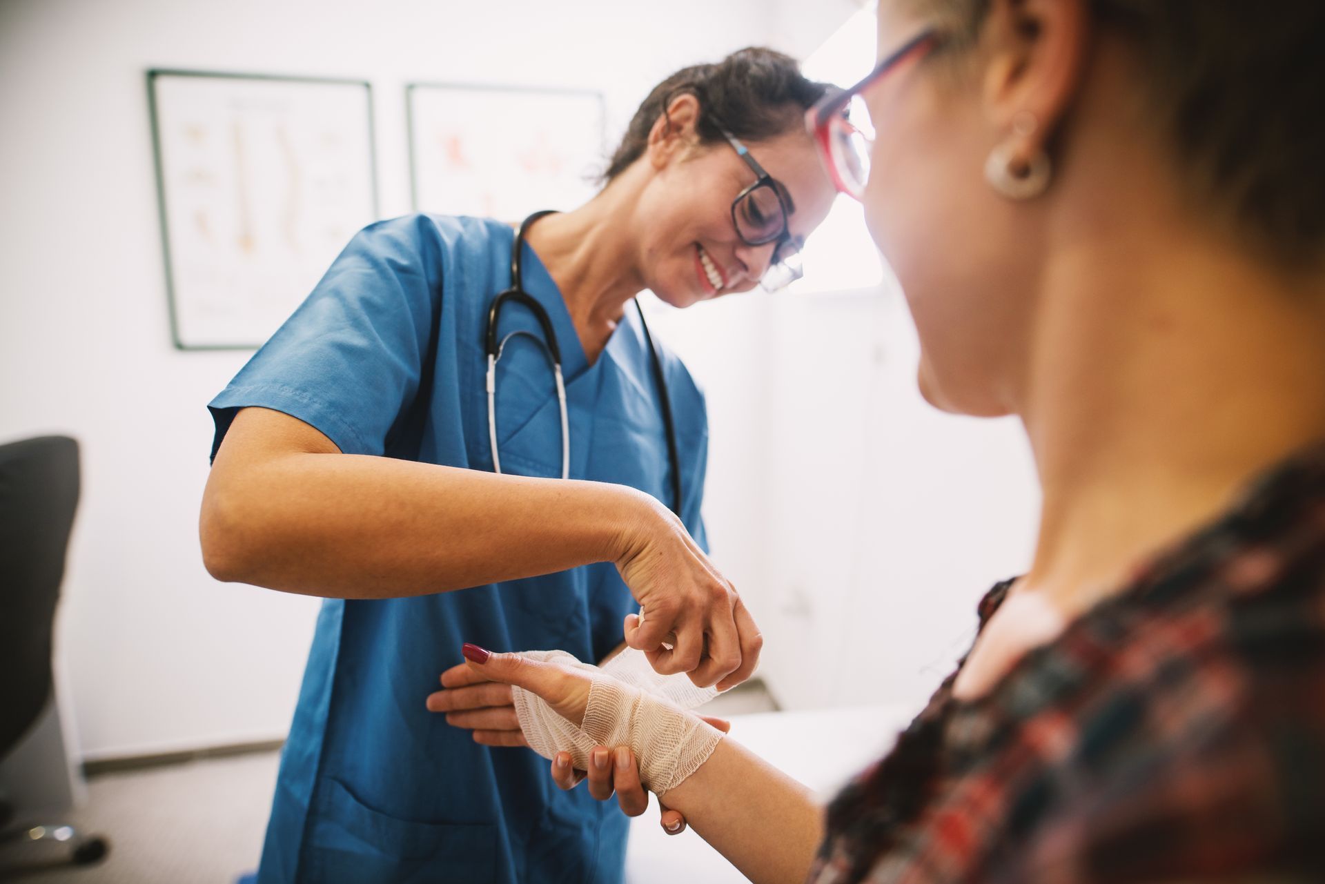 Nurse wrapping bandage around a patient's injured wrist in a doctor's office.