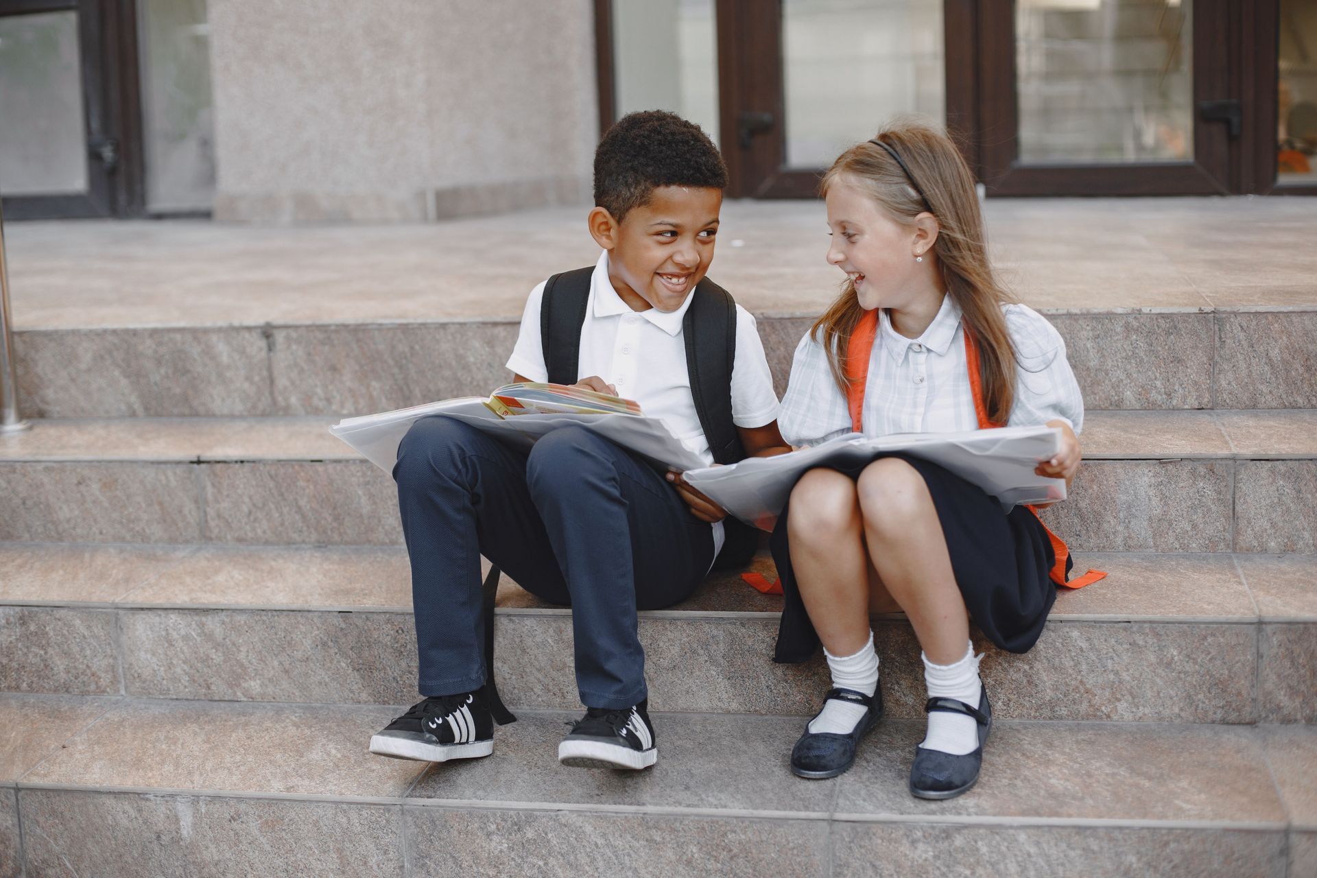 Two schoolchildren sitting on steps and reading books together outdoors