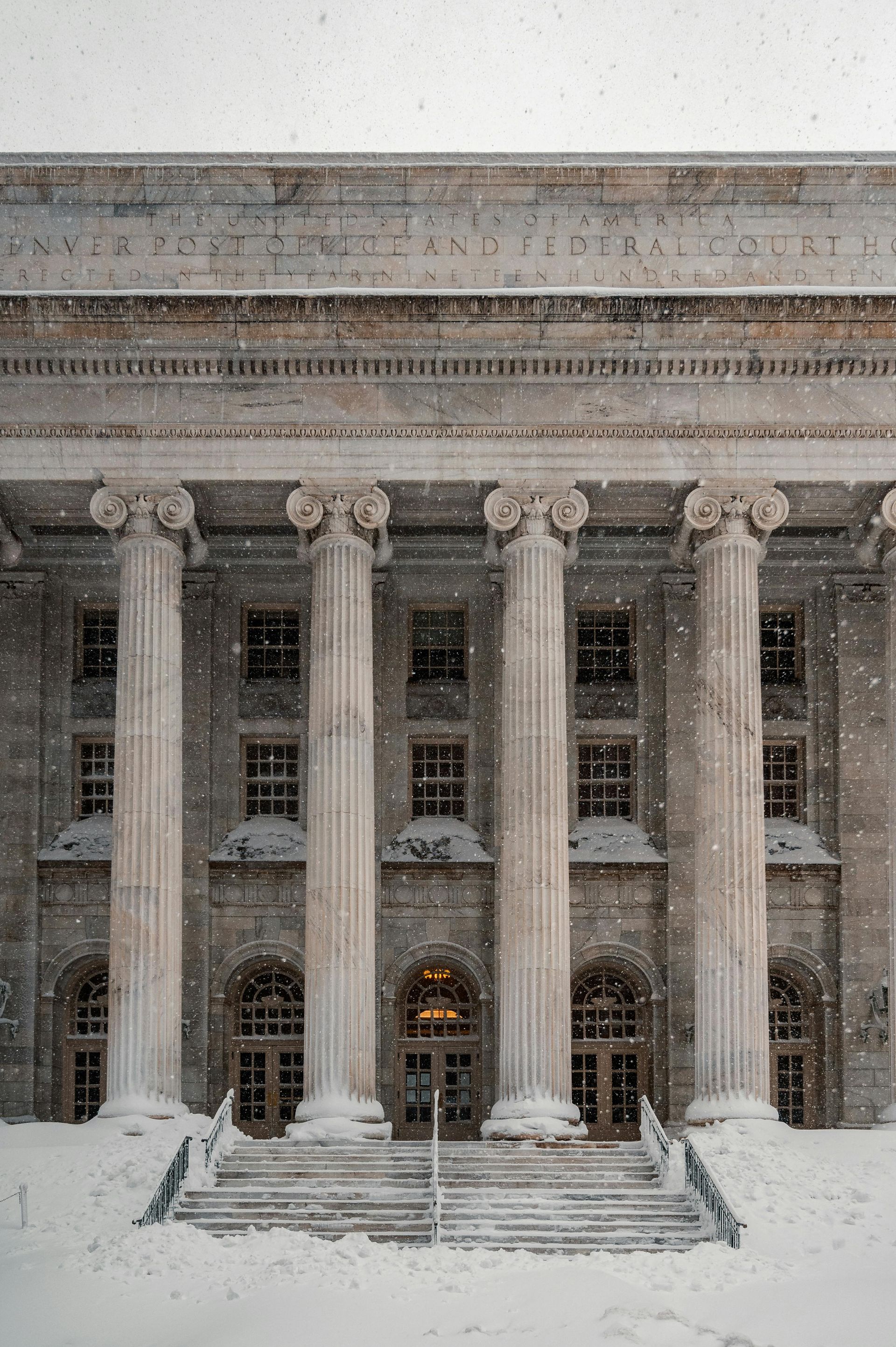 Snow-covered neoclassical building facade with tall columns and lit entrance steps