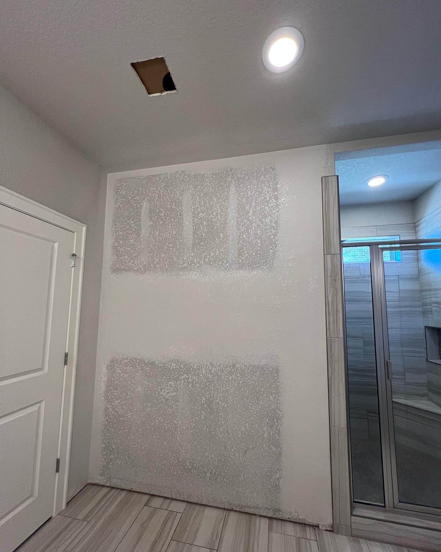 Bathroom with drywall repair; open ceiling access, partially finished walls, and a glass shower enclosure.