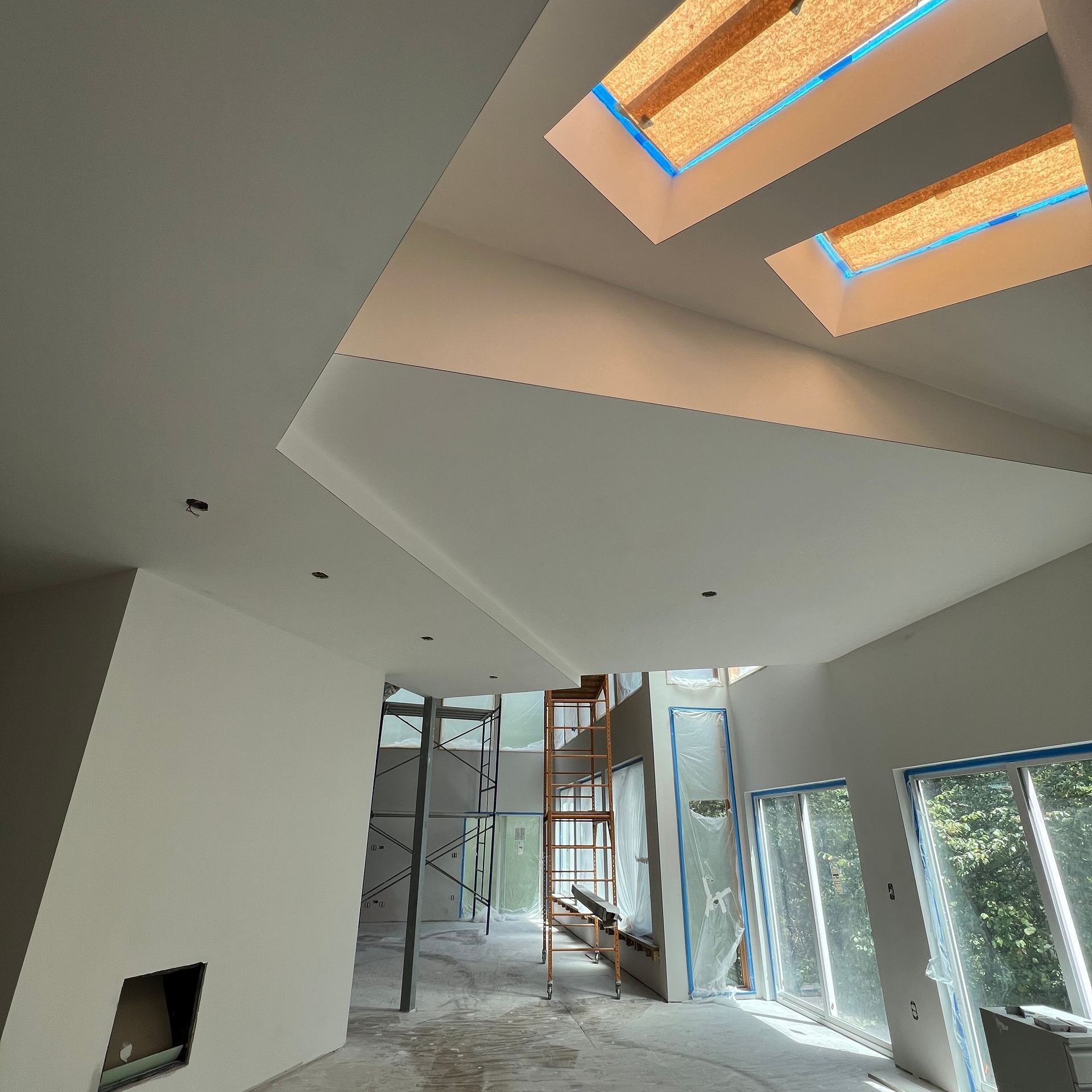 Interior view of a modern space under construction, featuring skylights, scaffolding, and large windows.