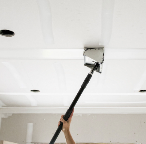 Person using a drywall taping tool to finish the ceiling, white paint visible.
