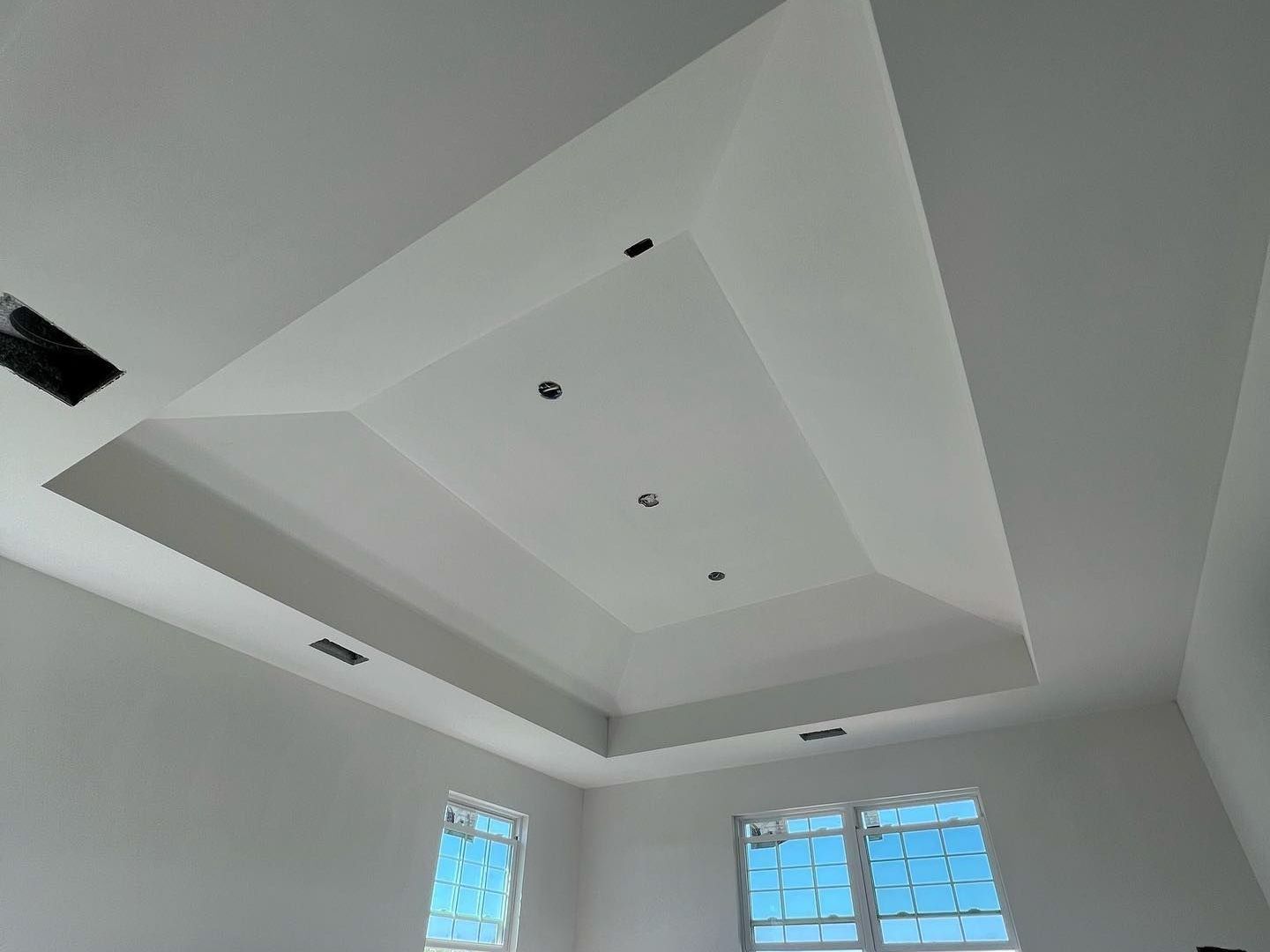 White ceiling with tiered design and recessed lighting in a room with windows.