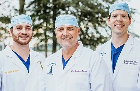 Three doctors in white coats and blue caps smiling outdoors