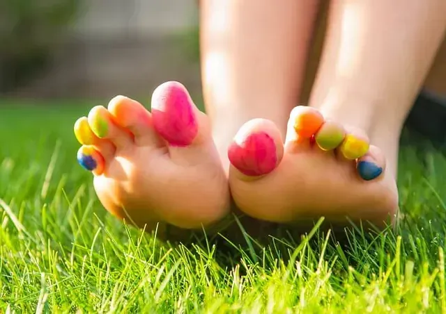 Bare feet with brightly painted toenails resting on green grass