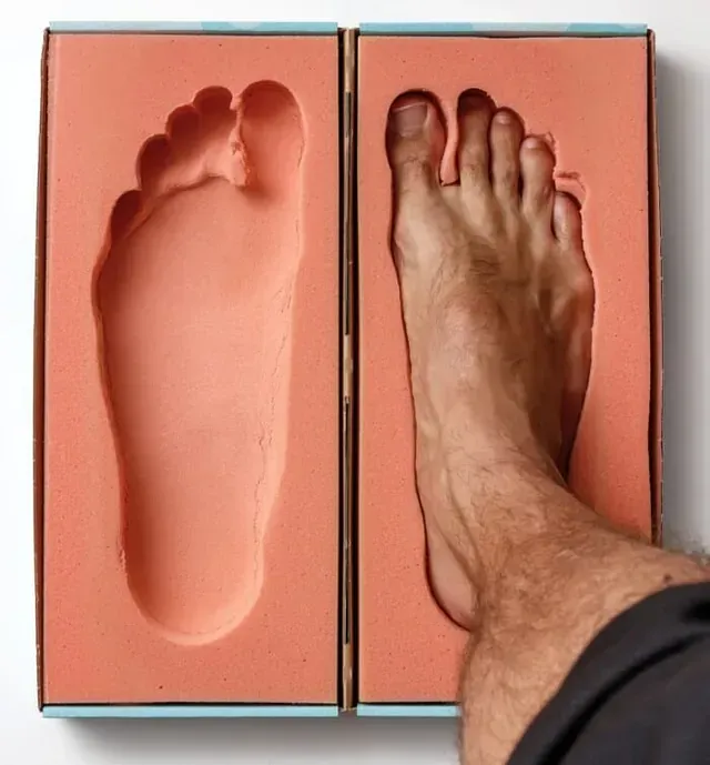 Foot stepping onto a coral foot-shaped mold next to an empty matching mold.