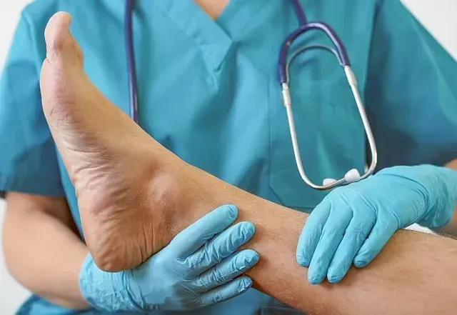 Healthcare worker examining a patient’s foot with gloved hands and stethoscope in a clinical setting