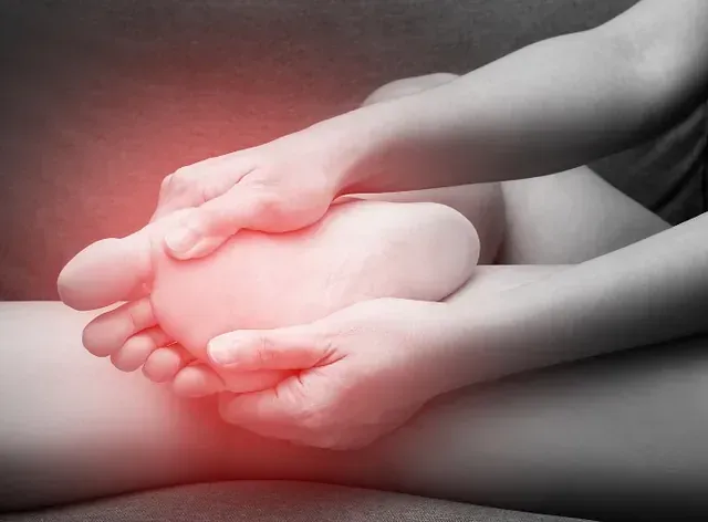 Hands gently holding a bare foot with a red pain glow on the heel/sole