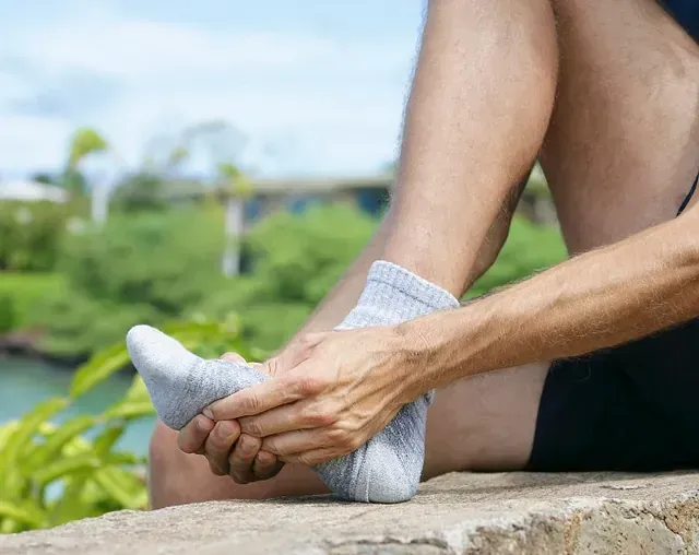 Person stretching foot outdoors on a stone ledge, wearing white socks with green scenery in the background