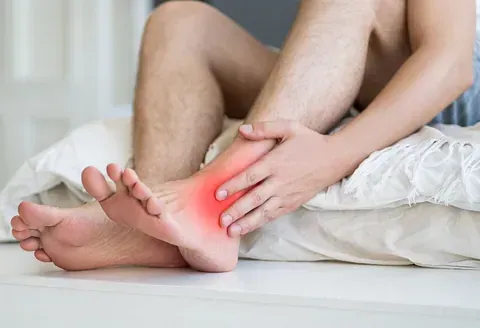 Person holding a glowing red ankle while seated on a bed