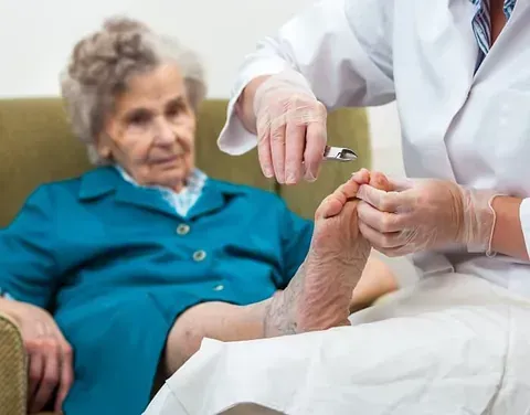 Healthcare worker trimming an elderly patient's toenails while seated on a couch