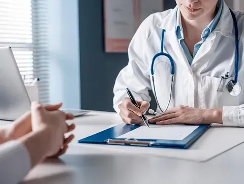 Doctor writing on a clipboard during a consultation across a desk