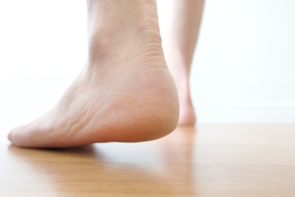 Bare feet standing on a wooden floor, one heel raised near the camera.