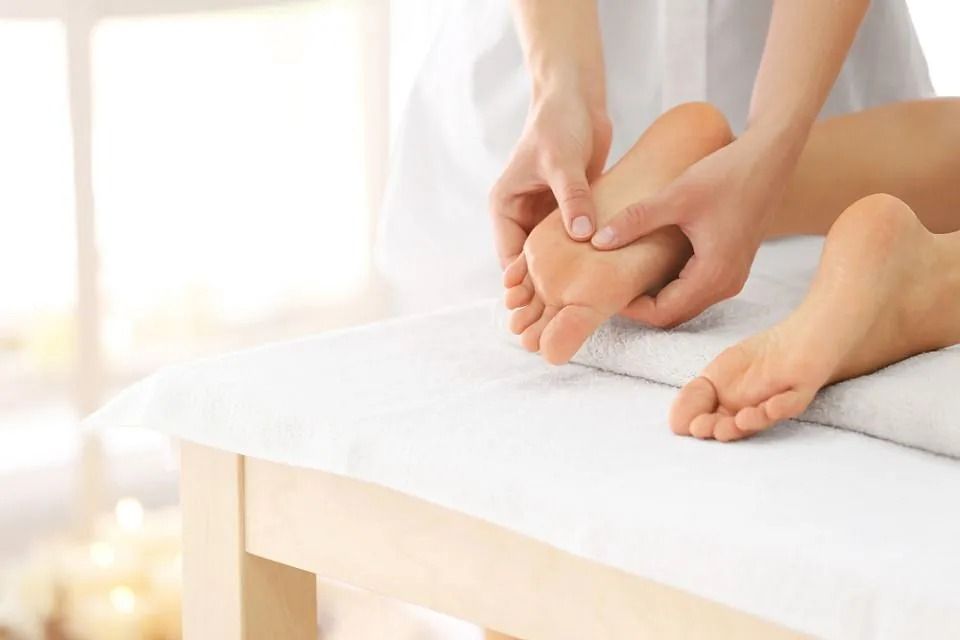 Hands massaging a person’s foot on a white treatment table in a bright spa setting