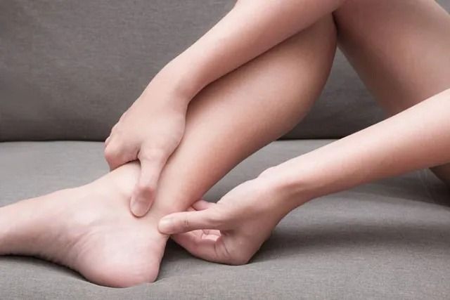 Hands massaging an ankle and foot on a gray couch