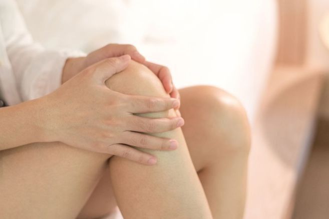 Close-up of hands clasped around a bent knee on a soft, bright couch