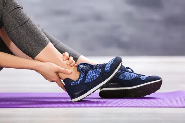 Person tying blue athletic shoe on purple yoga mat