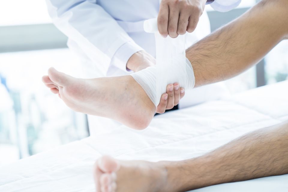 Doctor wrapping a patient’s ankle with a white bandage in a bright clinic room