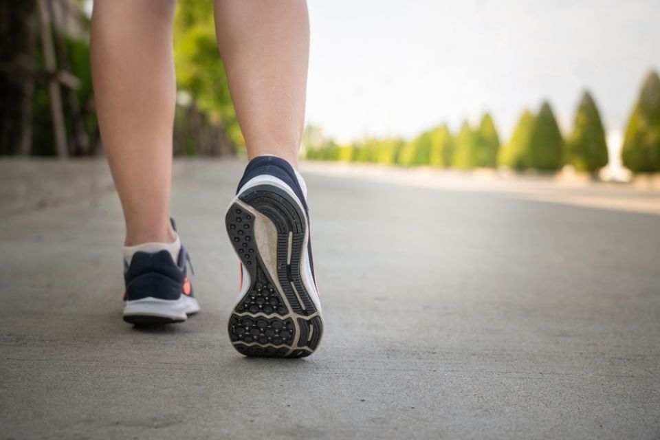 Runner’s feet from behind on a paved road, wearing black sneakers with white soles.