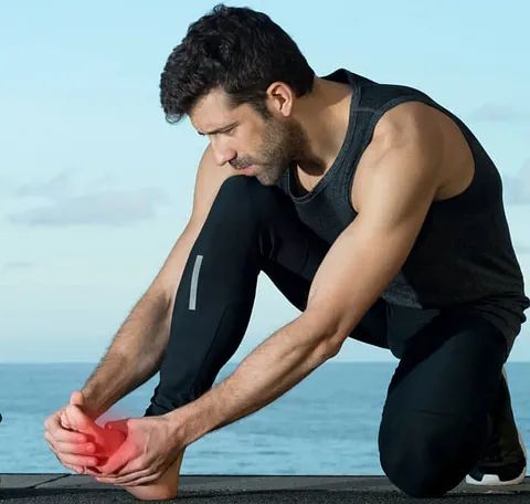 Man in black athletic wear stretching his leg on a boardwalk by the sea