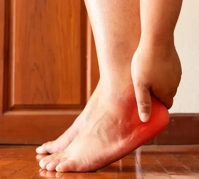 Hand clutching the heel of a foot, indicating ankle pain.