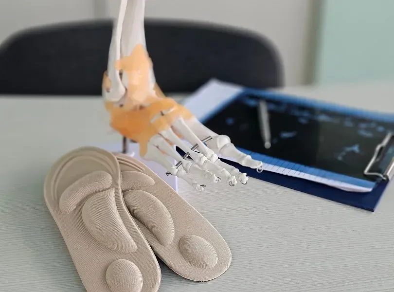 3D-printed ankle joint model with beige insoles and a tablet on a desk