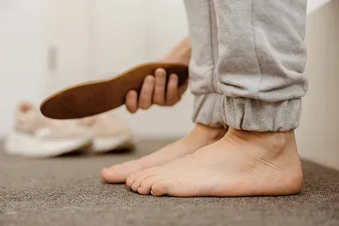 Person holding a brown shoe near bare feet on a carpeted floor