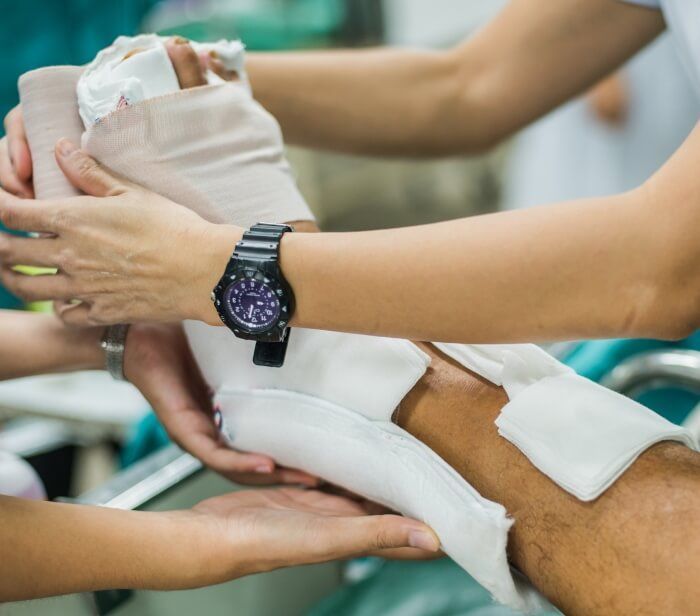 Bandaged injured leg being supported by hands in a medical setting