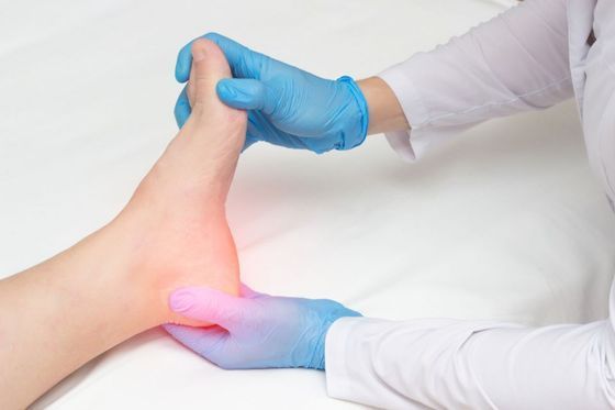 Gloved clinician examining a patient’s foot with a red-lit painful area on the heel