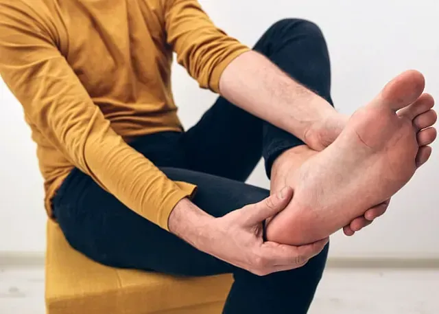 Person sitting on a yellow chair, holding a bare foot and ankle with both hands