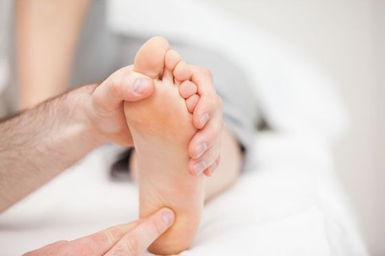 Hands massaging a bare foot on a white bed.