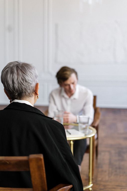 Two people talking across a small table in a bright, minimalist room.