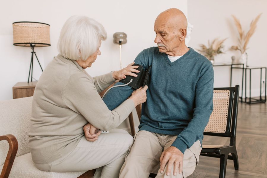 Caregiver checking an older adult’s blood pressure at home on a couch