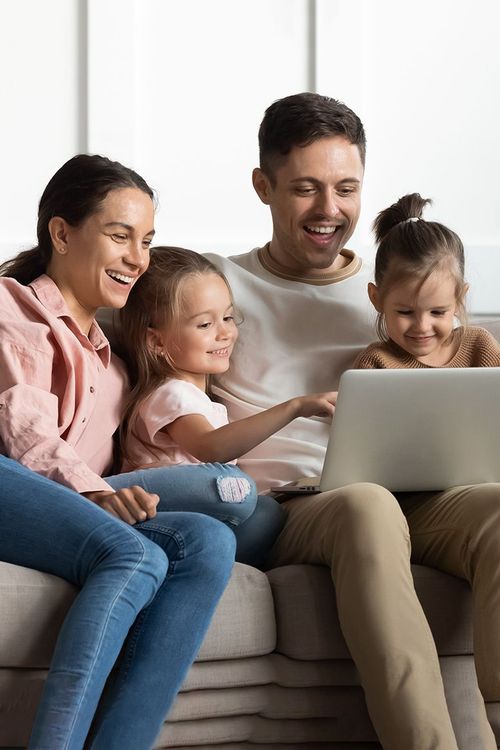 Family sitting on a couch together, smiling and looking at a laptop