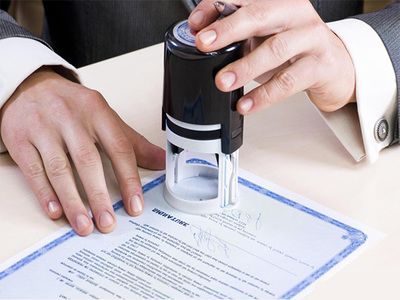 Hands stamping a document with a black self-inking stamp on a desk