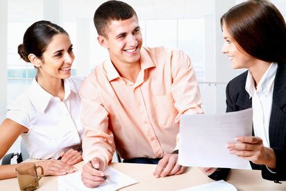 Three colleagues in a meeting, smiling and reviewing documents at a table